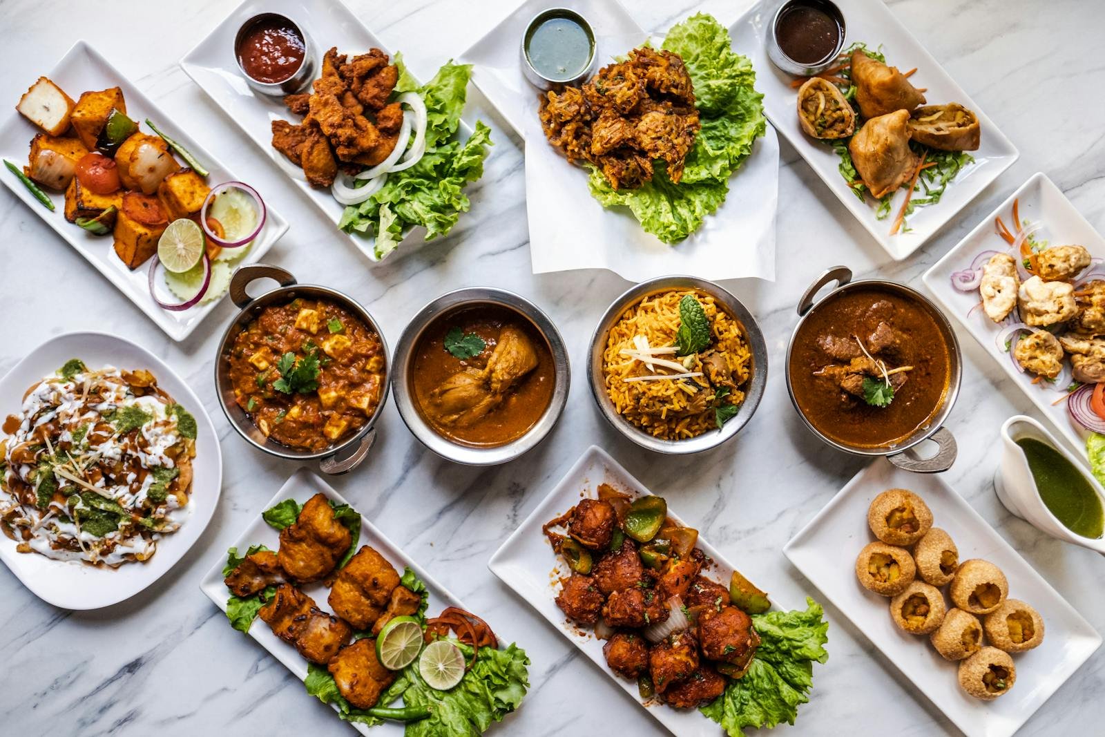 An overhead view of a variety of Indian dishes presented on white plates, highlighting vibrant colors and rich textures.